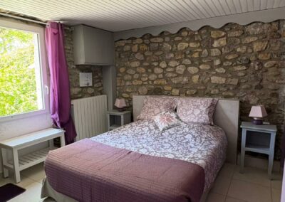 Chambre d'hôtes Améthyste avec lit double et mur en pierres apparentes au Mas de la Colombe à Grospierres.